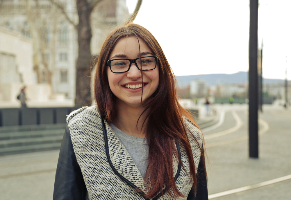 teenager with black glasses smiling outside